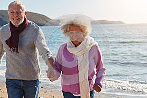 Active Senior Couple Running Along Winter Beach By Waves Holding Hands