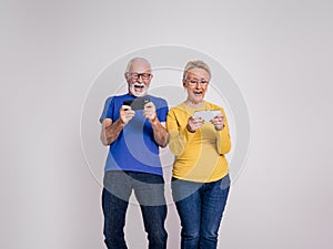 Active senior couple shouting cheerfully and playing video games over cellphones on white background