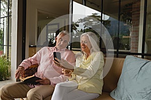 Active senior couple using mobile phone and reading a book in the porch