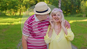 Active senior grandfather pensioner walking to stylish grandmother and making a kiss in summer park