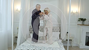 Active senior grandparents couple jumping on bed at home. Woman and man enjoying life in retirement