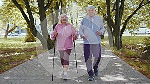 Active senior grandparents training Nordic walking with ski trekking poles, running in summer park