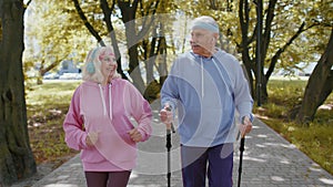 Active senior grandparents training Nordic walking with ski trekking poles, running in summer park