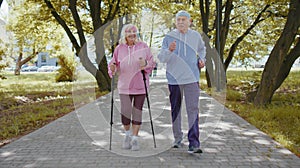 Active senior grandparents training Nordic walking with ski trekking poles, running in summer park