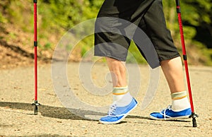 Active senior legs in sneakers nordic walking in a park.