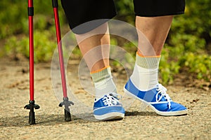 Active senior legs in sneakers nordic walking in a park.