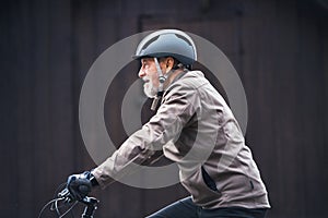 Active senior man with bike helmet cycling outdoors againts dark background.
