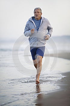 Active senior man jogging along the beach