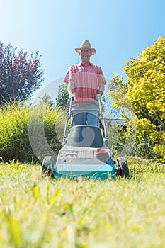Active senior man smiling while using a grass cutting machine in the garden