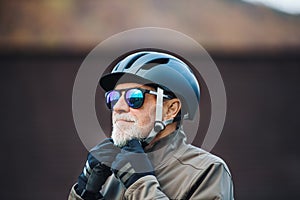 An active senior man standing outdoors in town, putting on a bike helmet.