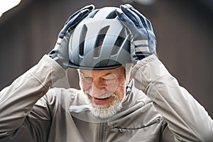 An active senior man standing outdoors in town, putting on a bike helmet.