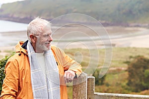 Active Senior Man Walking Along Coastal Path In Fall Or Winter By Gate With Beach And Cliffs Behind