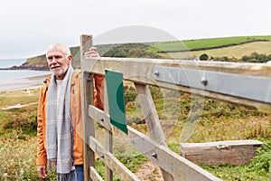 Active Senior Man Walking Along Coastal Path In Winter Opening Gate With Beach And Cliffs Behind