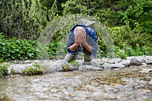 Active senior man washing his face in mountain stream.