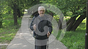 Active senior old man training Nordic walking with ski trekking poles in park