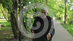 Active senior old man training Nordic walking with ski trekking poles in park