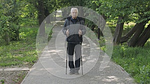 Active senior old man training Nordic walking with ski trekking poles in park