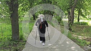 Active senior old woman in mask training Nordic walking in park at quarantine