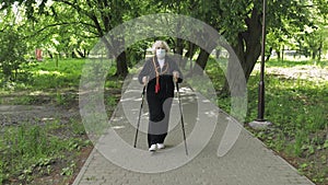 Active senior old woman in mask training Nordic walking in park at quarantine