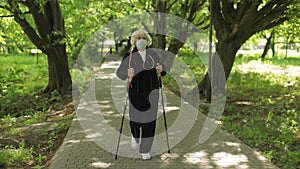 Active senior old woman in mask training Nordic walking in park at quarantine