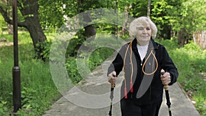 Active senior old woman training Nordic walking with ski trekking poles in park