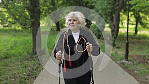 Active senior old woman training Nordic walking with ski trekking poles in park