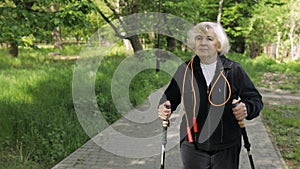 Active senior old woman training Nordic walking with ski trekking poles in park