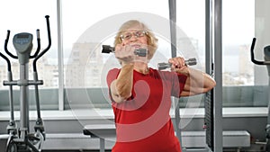 Active senior retired woman with barbells in gym. Active and happy old years concept. Positive retired person making