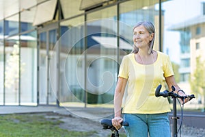 Active senior retired woman walks outside a modern building with a bicycle