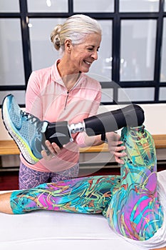 Active senior woman assisting disabled woman to stretching leg in sports center