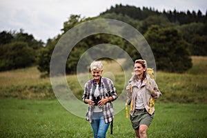 Active senior woman with binoculars hiking with her adult daughter outdoors in nature.