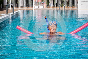 Active senior woman doing exercise in swimming pool with swim noodles. Happy retired people in the outdoor pool water under the