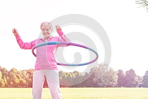 Active senior woman doing gymnastic with hula hoop in park