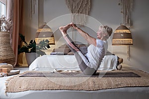 Active senior woman doing yoga training at home, holding navasana or boat yoga pose