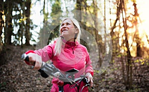 Active senior woman with e-bike cycling outdoors in nature.