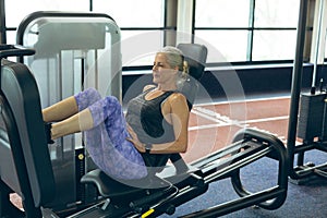 Active senior woman exercising with leg press machine in fitness studio