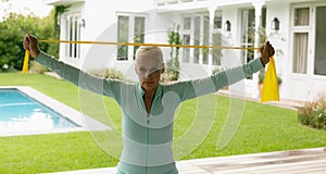 Active senior woman exercising with resistance band in porch at home
