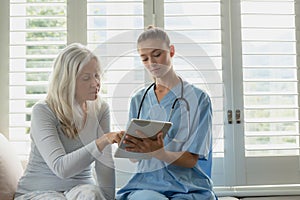 Active senior woman and female doctor using digital tablet on window seat