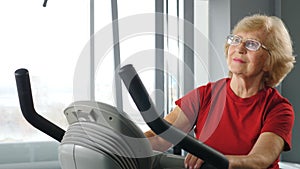 Active senior woman in gym. Female sportsmoman on bike in fitness studio. Old woman spinning bike on cycling class
