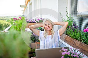 Active senior woman with laptop resting when working on balcony, home office.