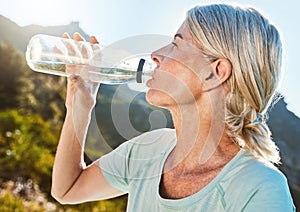Active senior woman out for a run or jog in nature and drinking water while taking a break. Living active and healthy