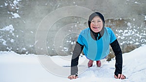 Active senior woman outdoors in snowy winter, doing push ups.