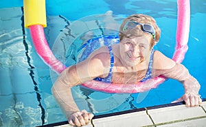 Active senior woman (over age of 50) in sport goggles, swimsuit doing aqua fitness with swim noodles.