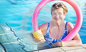 Active senior woman (over age of 50) in sport goggles, swimsuit, with swim noodles in swimming pool.