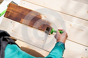 Active senior woman painting some pieces of wood, timber by brown paint colour with brush.worker painting a wooden wall
