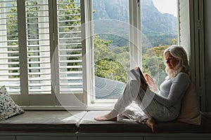 Active senior woman reading a book on window seat