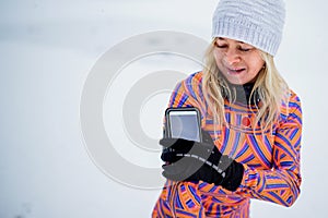 Active senior woman runner adjusting smartphone, attached to arm, for exercising outdoors in snowy winte.