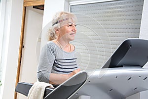 Active senior woman running on treadmill machine in the living room at home