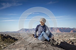 An active Senior woman sitting on a mountain top after hiking to the top