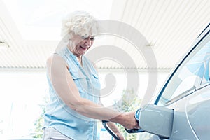 Active senior woman smiling while filling up the gas tank of her